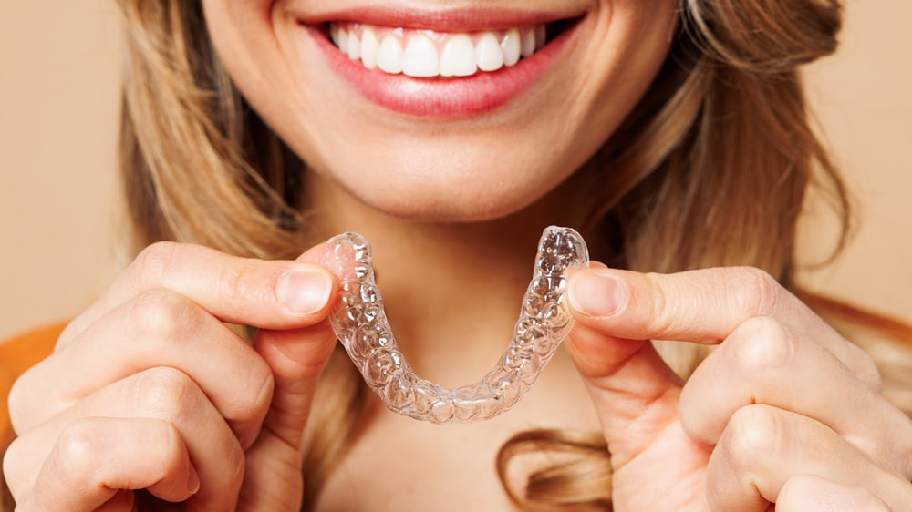 A woman confidently holds a clear aligner in her hand, symbolizing her commitment to dental alignment and oral health