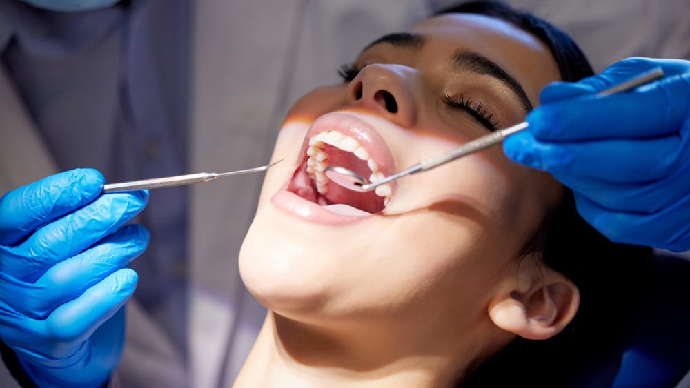 A dentist performs a teeth cleaning on a woman, utilizing Guided Biofilm Therapy for effective oral hygiene