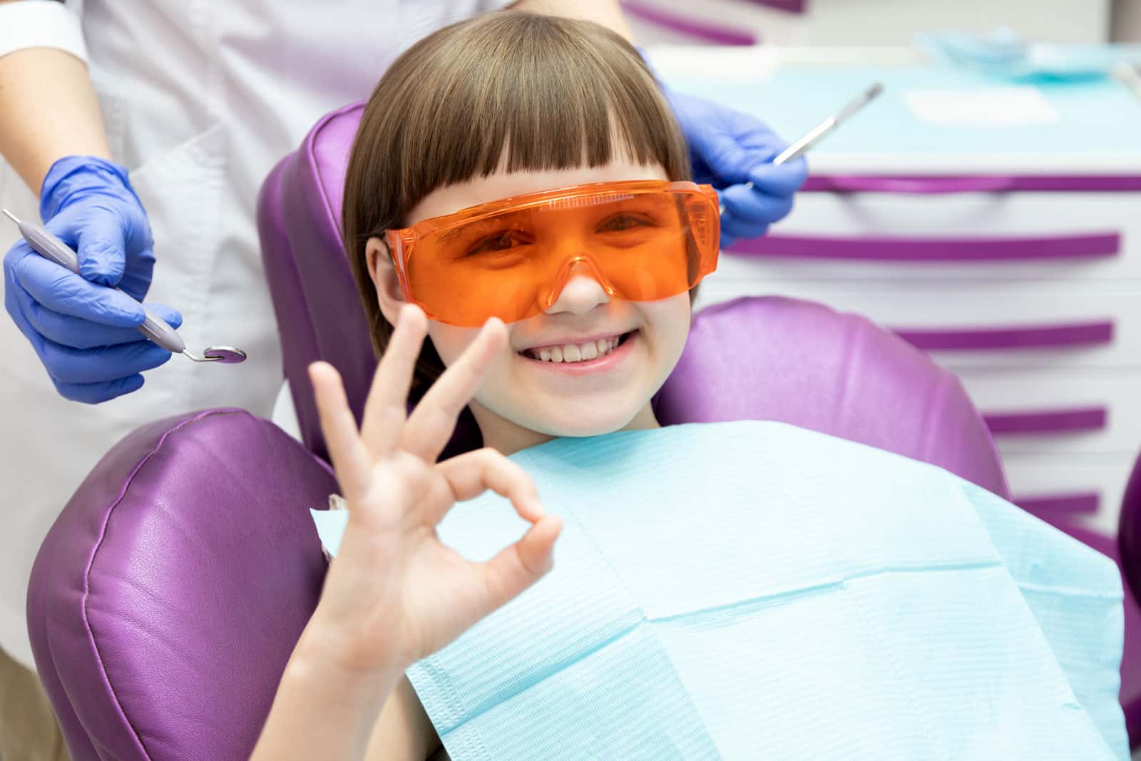 A young girl smiles brightly while seated in a pediatric dentist chair, showcasing a positive dental experience