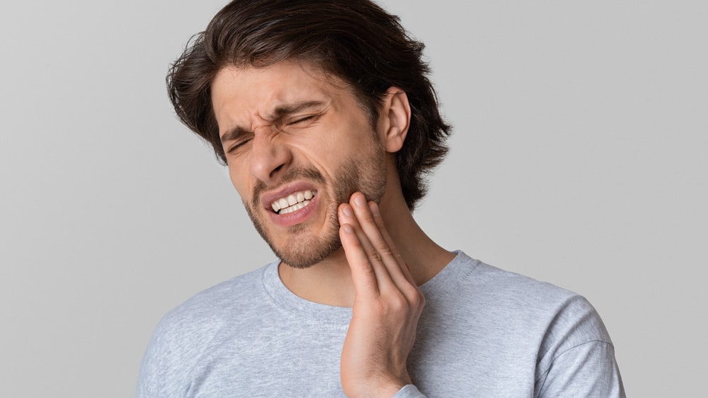 A man holding his cheek in pain, indicating discomfort from a toothache