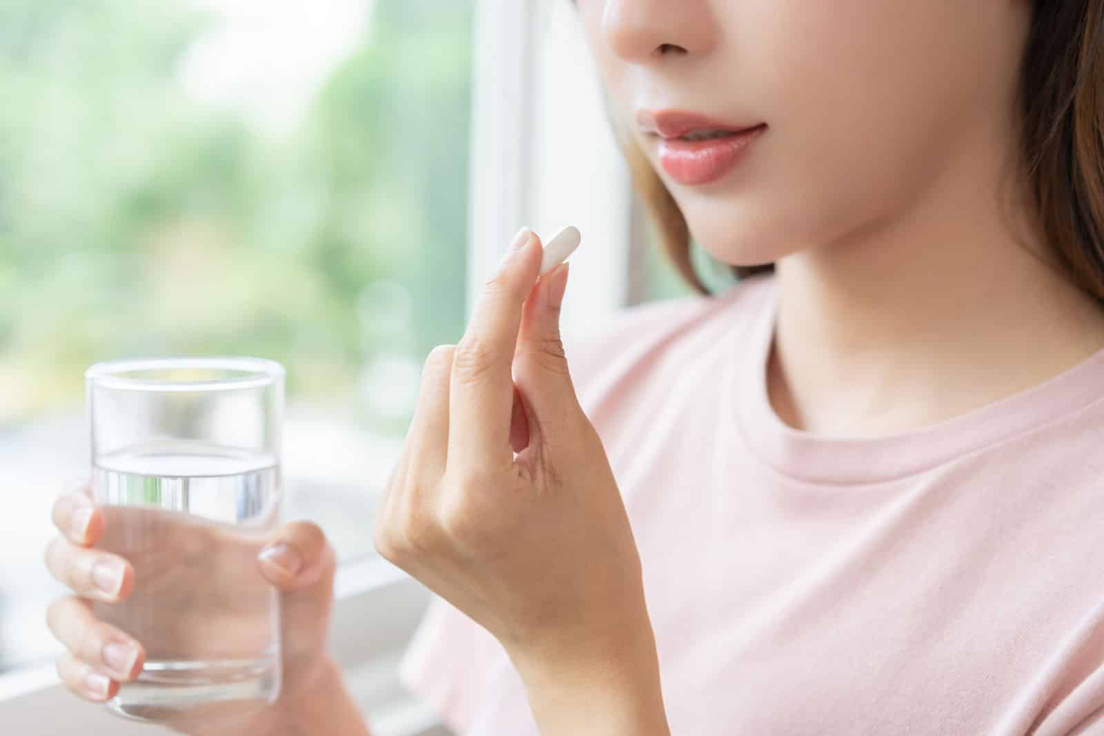 A woman looks at a glass of water with a pill in hand, symbolizing the process of oral sedation