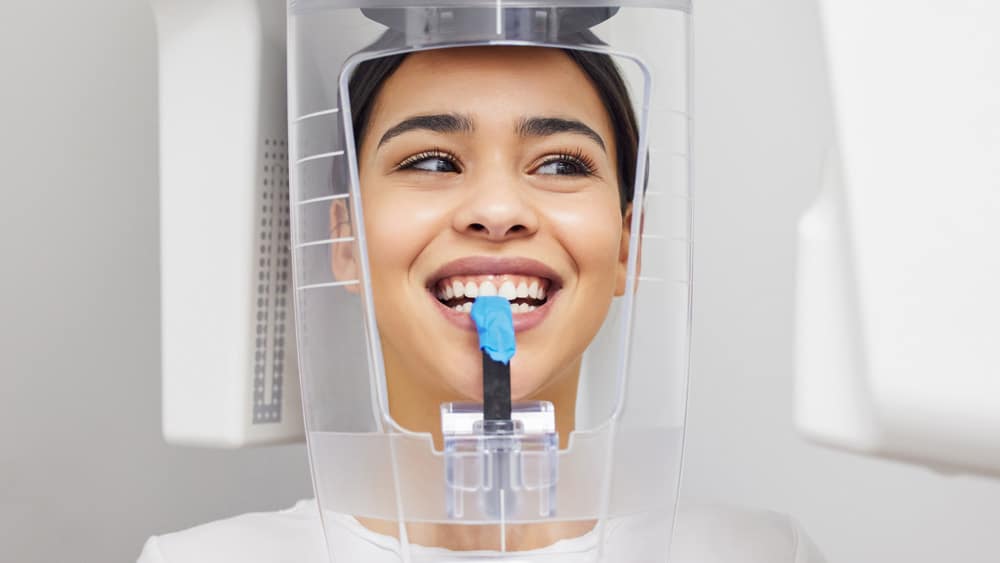 A woman smiles brightly while positioned in a CBCT scanner, preparing for advanced dental imaging to assess her oral health