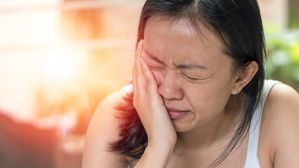 A woman holding her jaw in discomfort, seeking relief from jaw pain related to TMJ, highlighting the importance of effective TMJ solutions