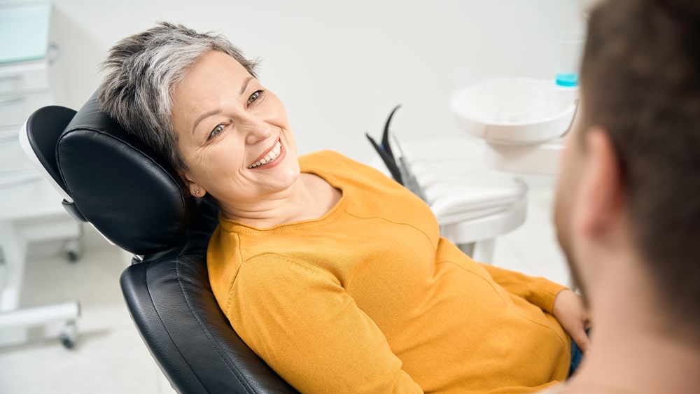 A woman in a dental chair undergoing a deep cleaning procedure, attended by a male dentist in a clinical environment