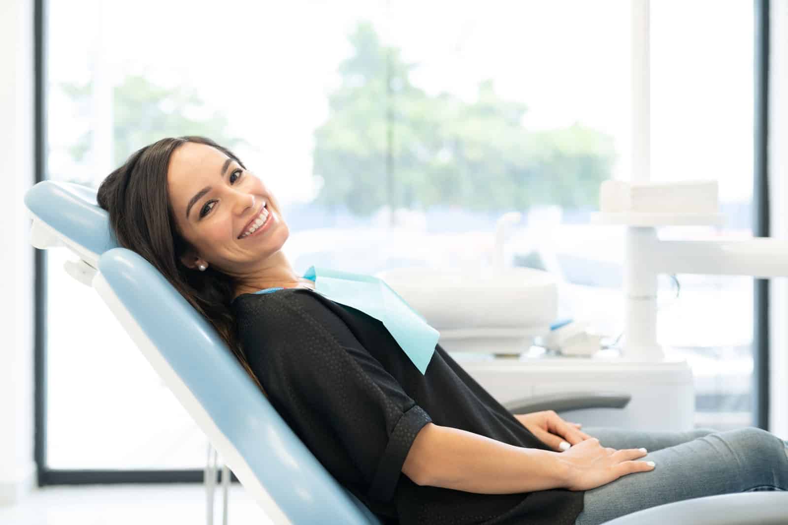 A woman in a dental chair smiles brightly, showcasing her satisfaction with the Airflow dental treatment