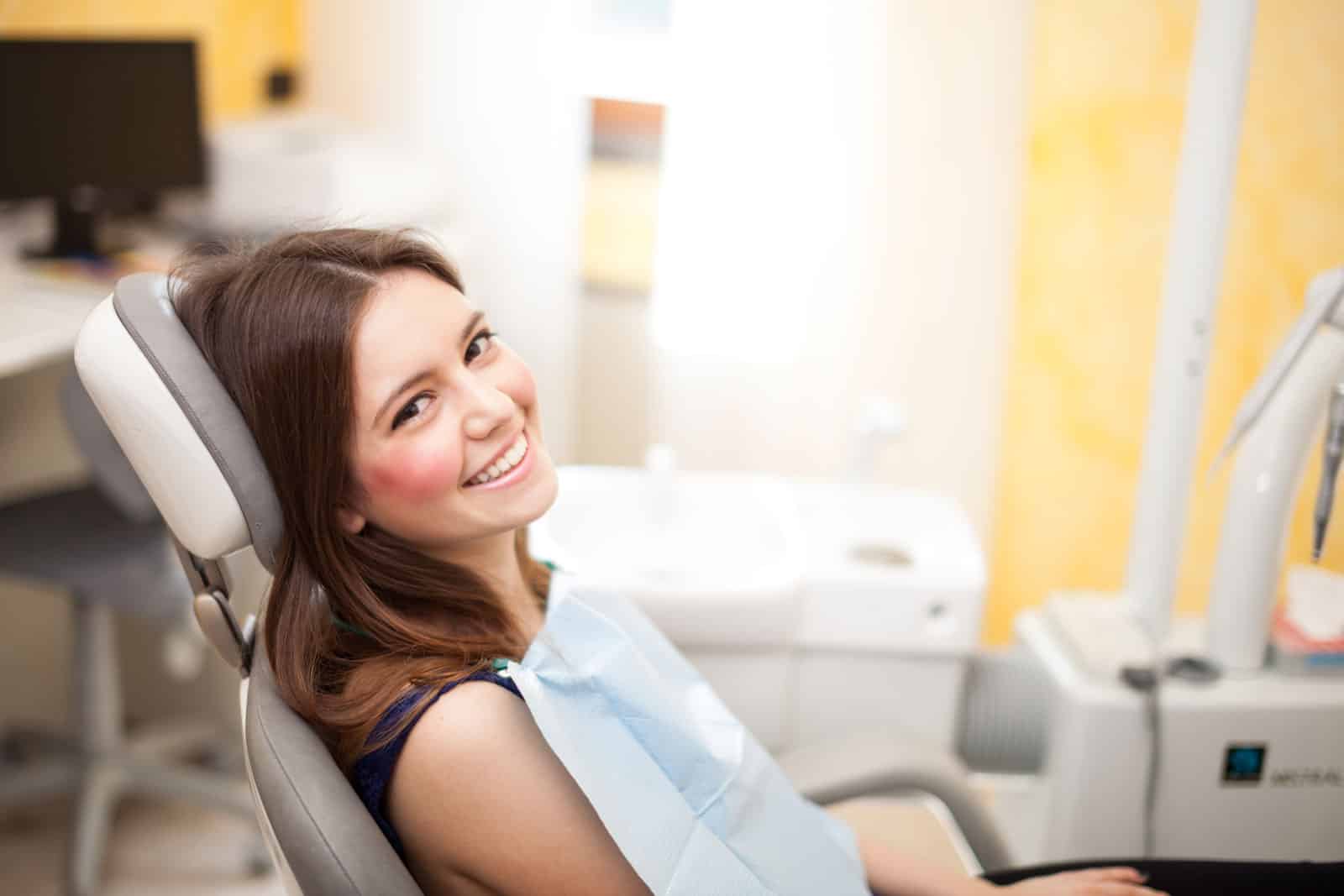 A woman smiles while seated in a dental chair, enjoying her routine cleaning appointment