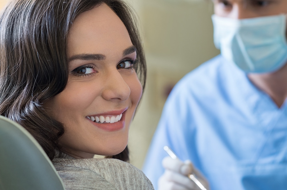 A woman smiling after a dental procedure with her dentist in the background, highlighting a successful dental visit